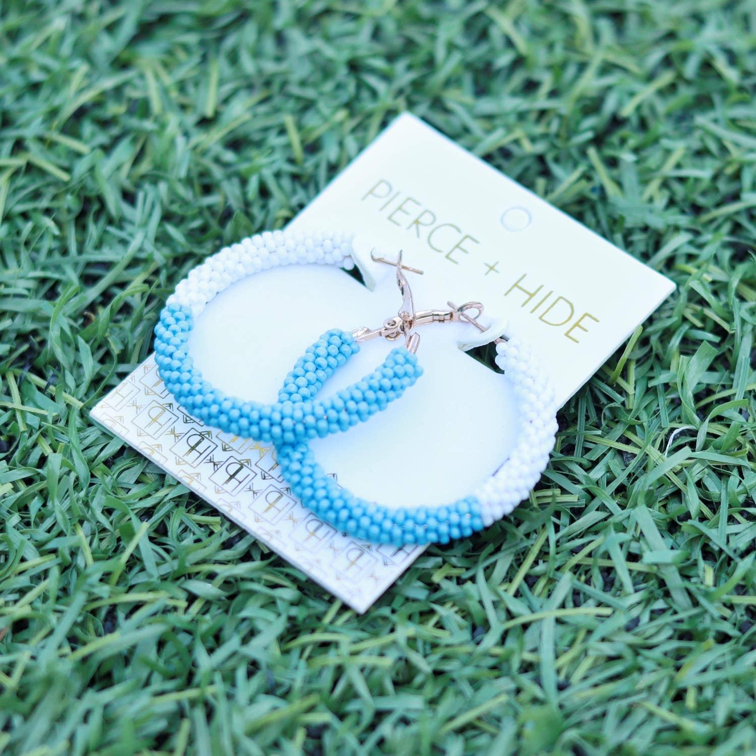 Blue and white beaded hoop earrings on display card, lying on green grass
