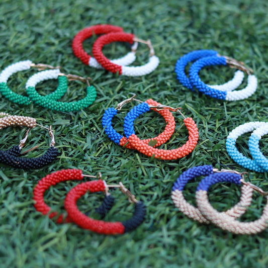 Colorful beaded hoop earrings in various patterns displayed on green grass