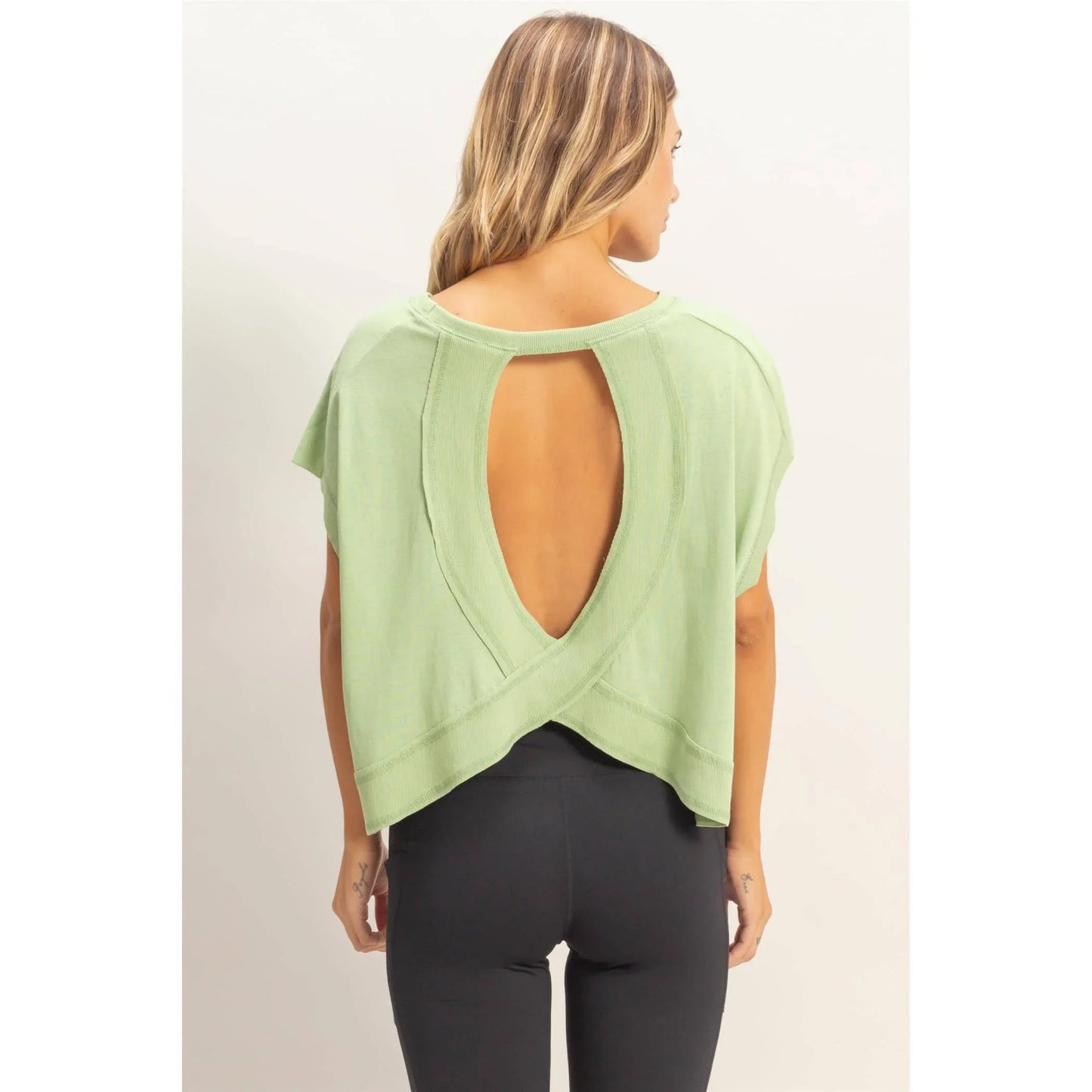 Woman wearing sage green open-back top with crisscross design and black leggings