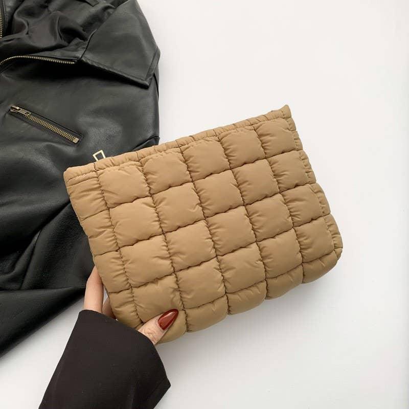 Hand holding quilted beige puffer clutch bag with black leather jacket background