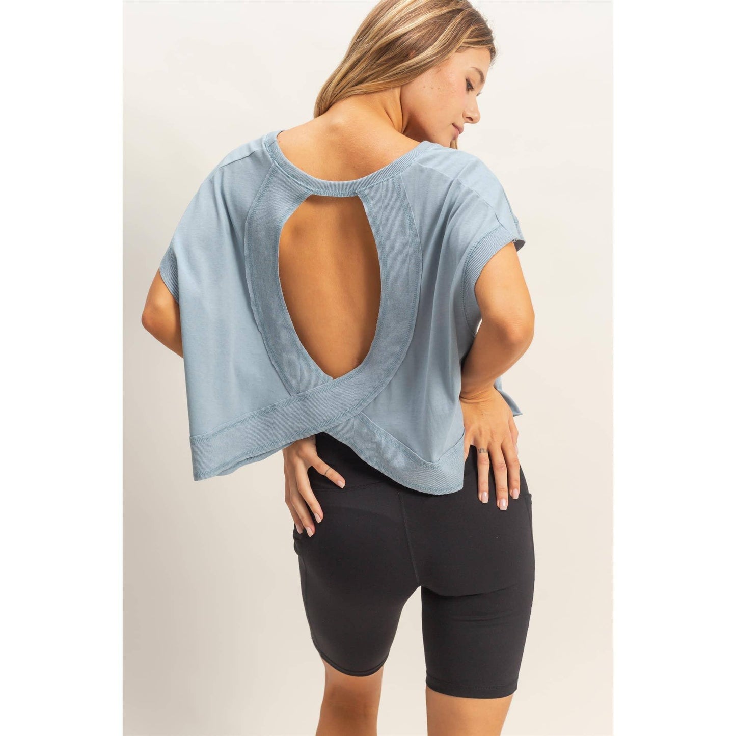 Woman wearing light blue open-back top and black biker shorts, posing in studio.