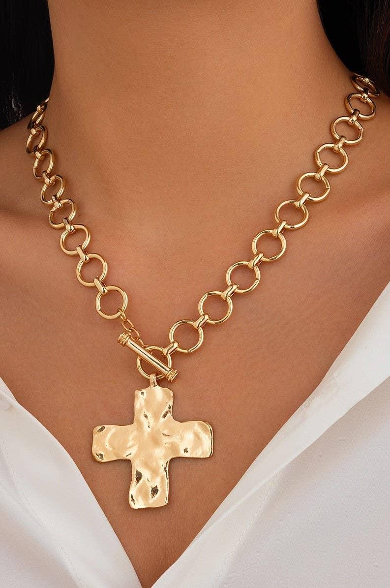 Chunky gold chain necklace with large hammered cross pendant on a woman's neck