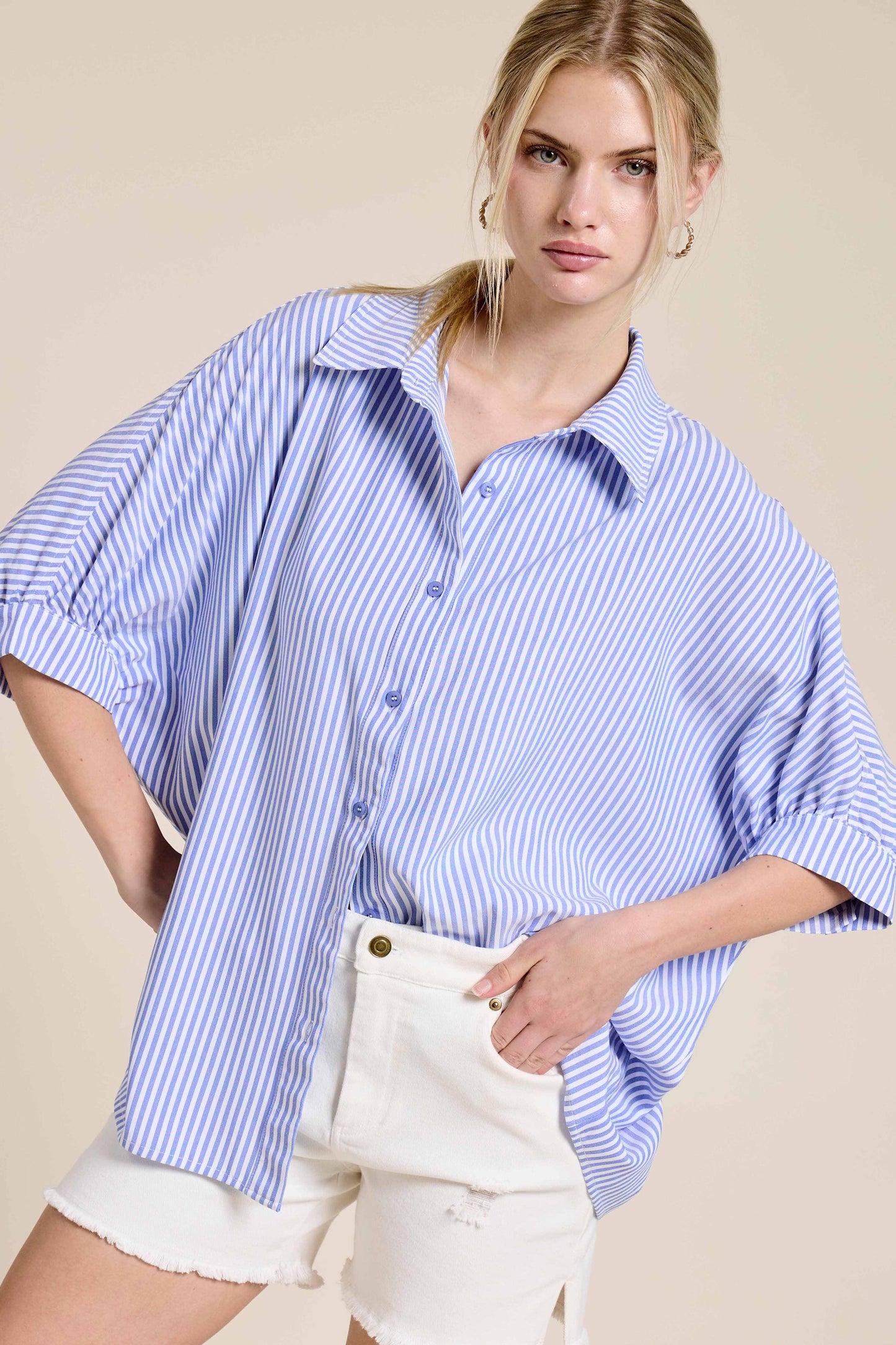 Woman wearing blue and white striped oversized button-up shirt with white denim shorts