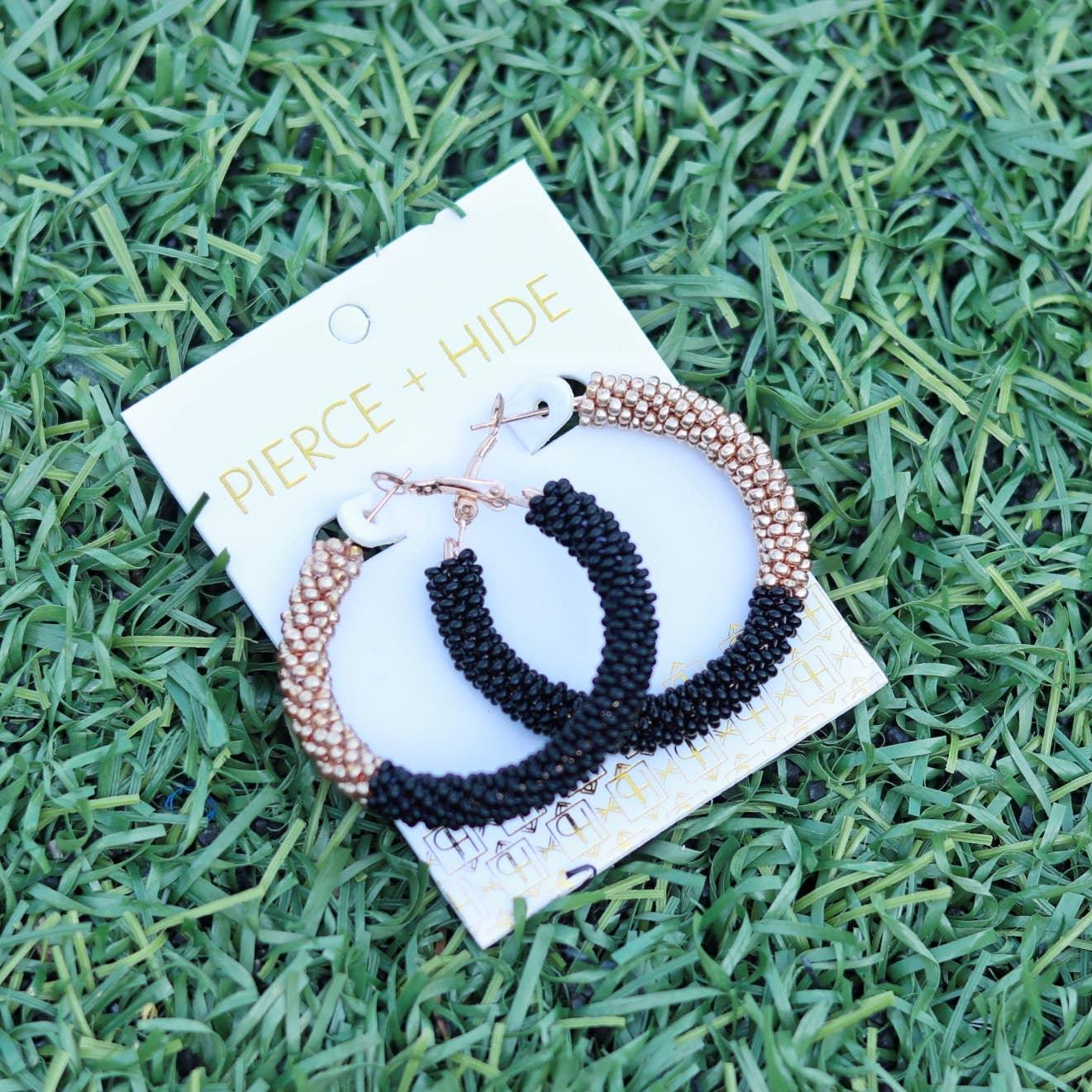 Black and gold beaded hoop earrings on display card, laying on green artificial grass