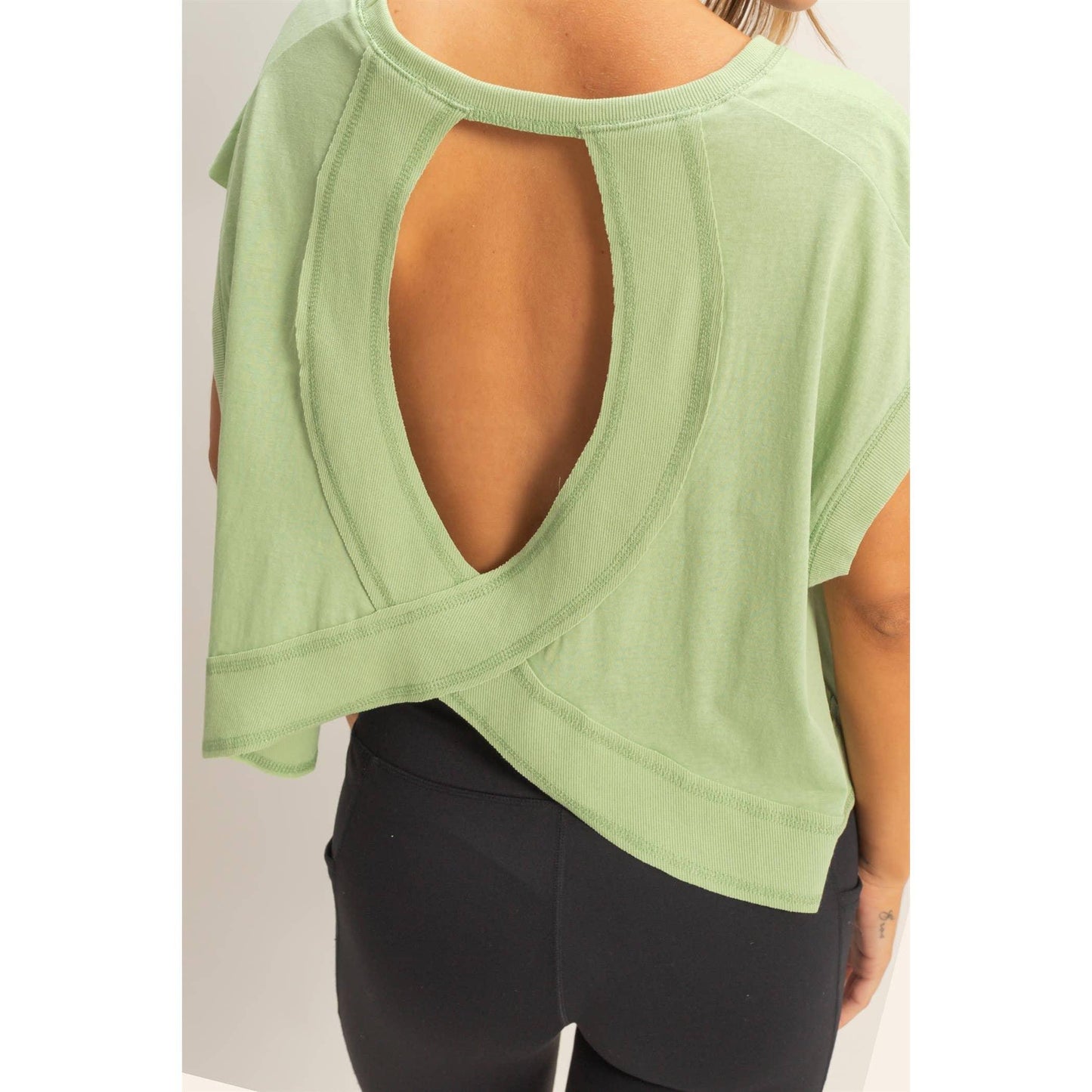 Woman wearing a light green open-back top with crisscross detail and black leggings