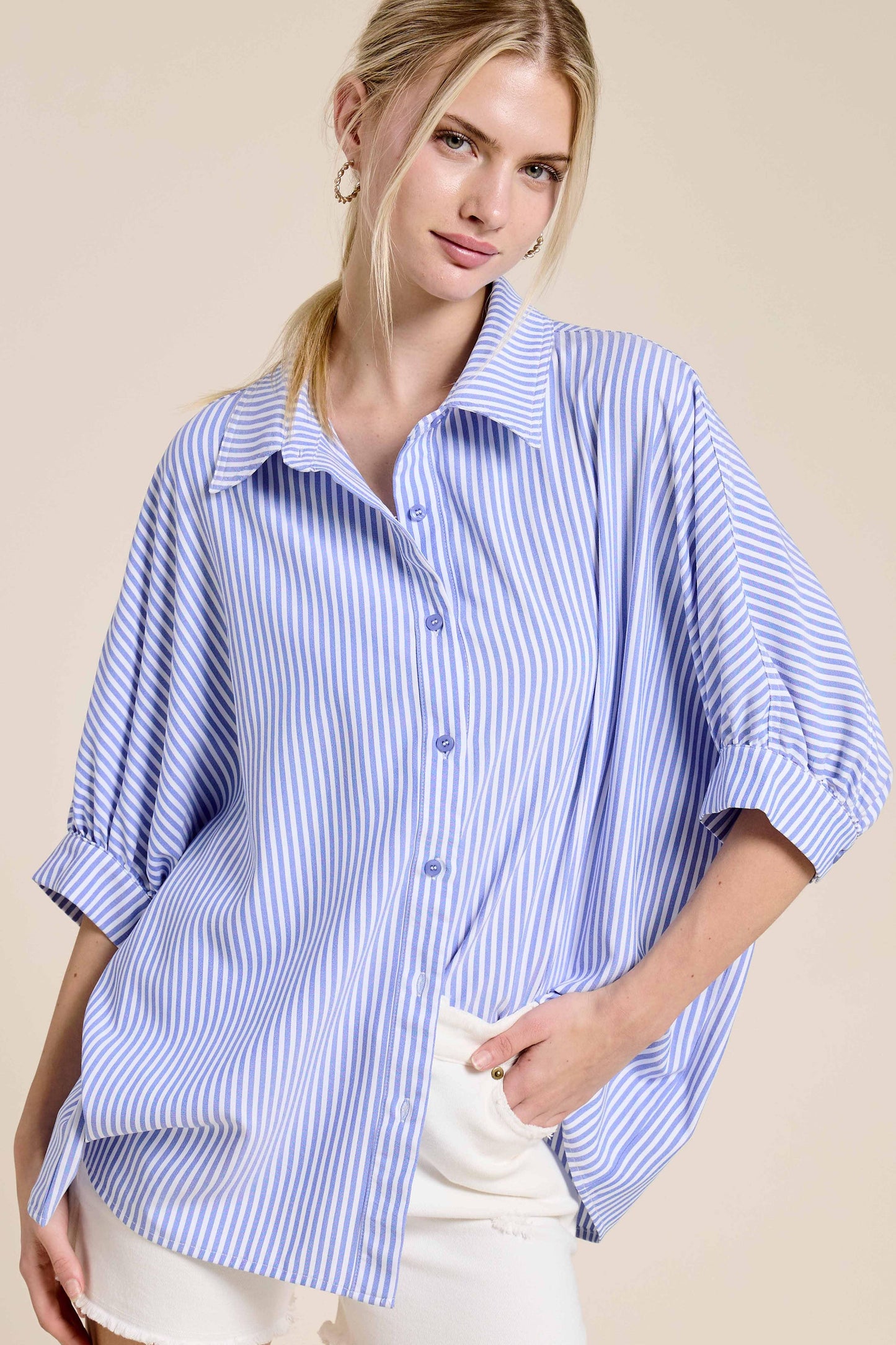 Woman wearing a loose blue and white striped button-up blouse with rolled sleeves and white shorts