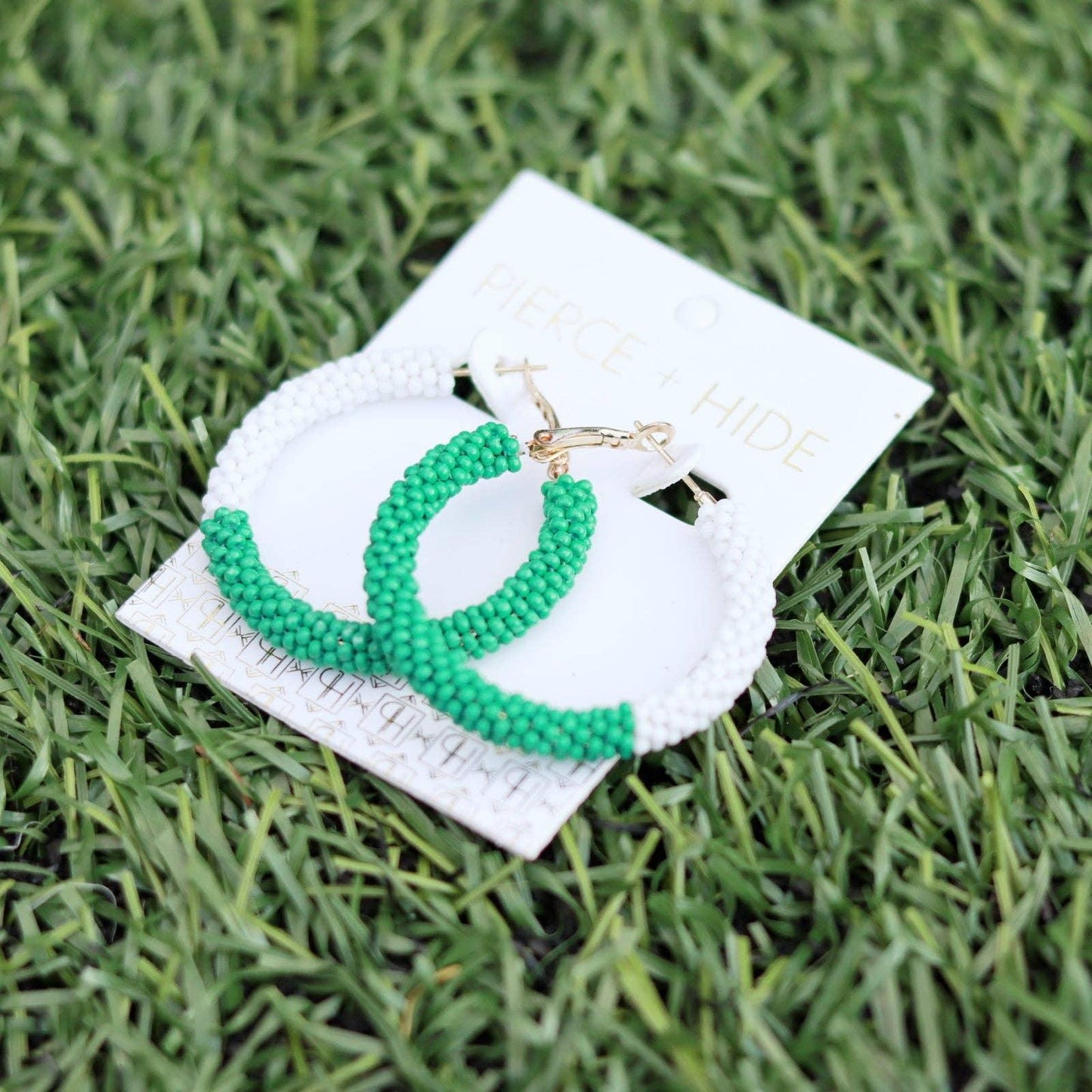 Green and white beaded hoop earrings on card, displayed on grass