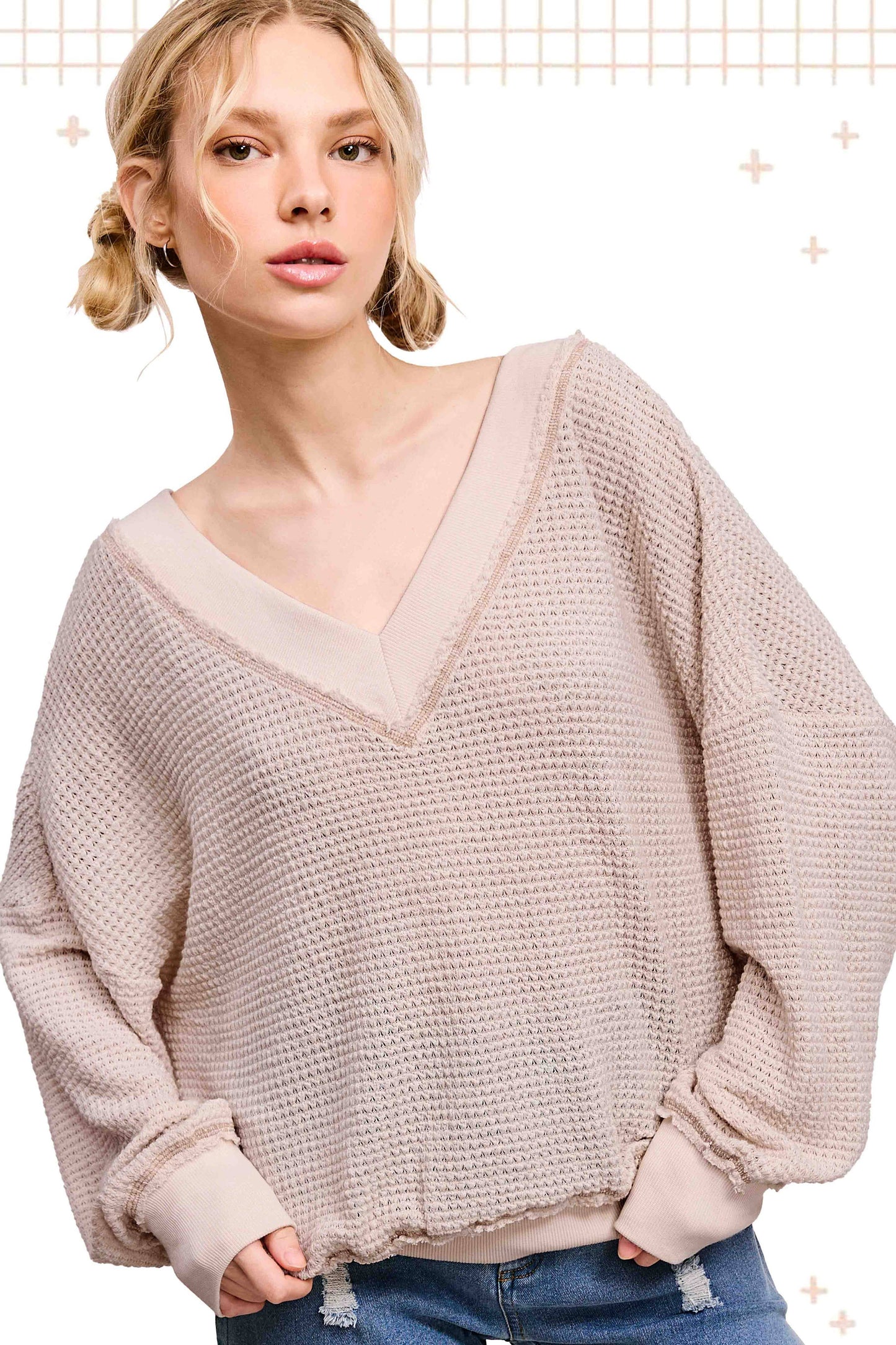 Woman wearing beige waffle knit V-neck sweater and blue jeans on white background