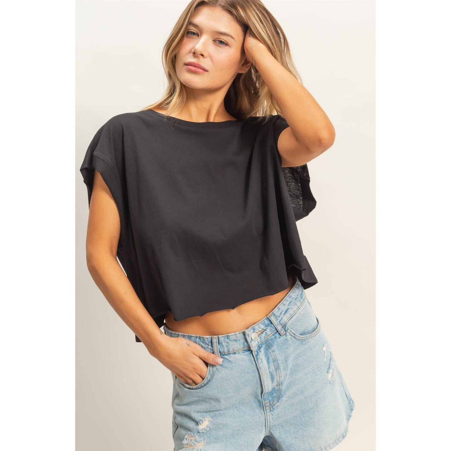 Woman wearing loose black crop top and light distressed denim shorts