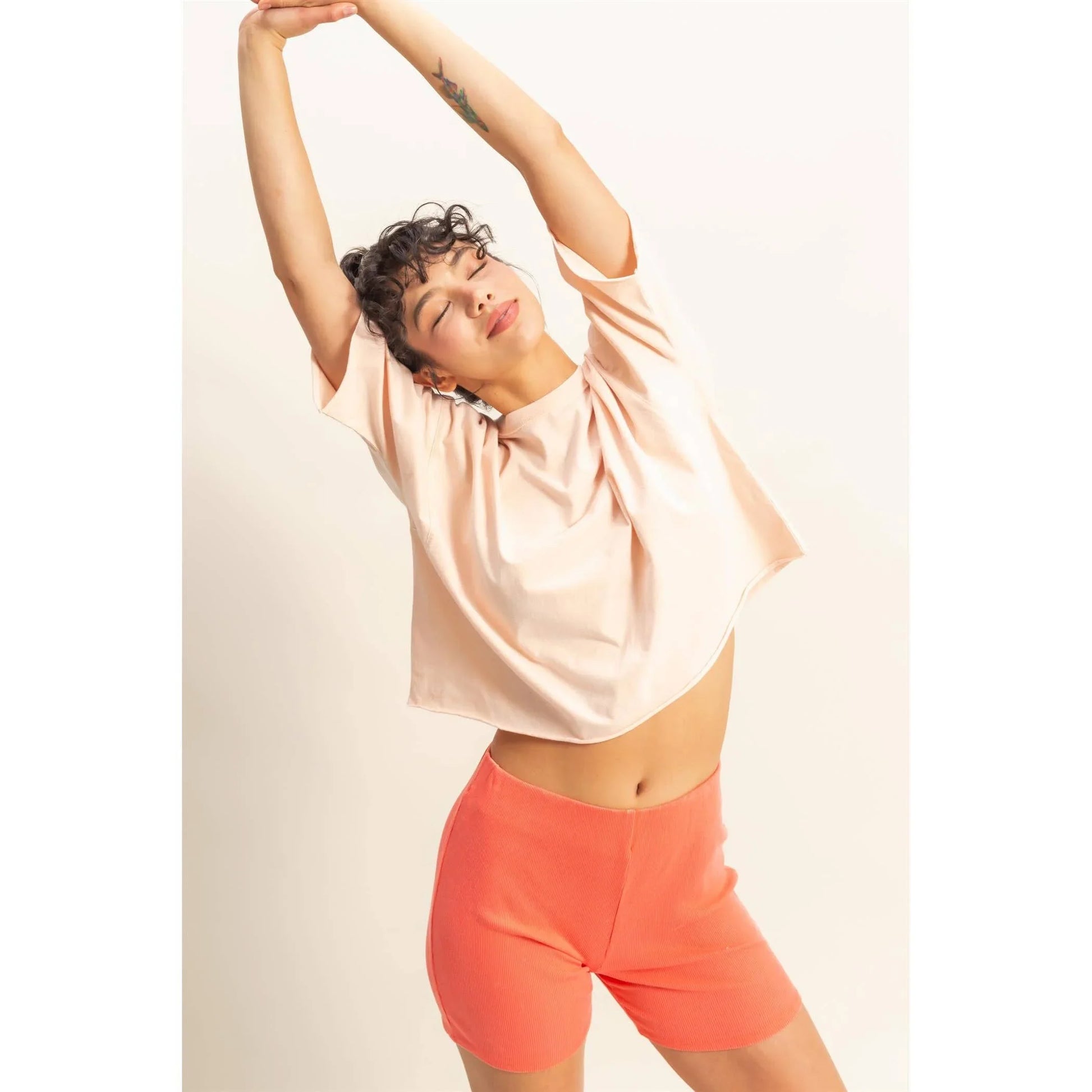 Woman in peach crop top and coral shorts stretching arms overhead, stylish casual outfit