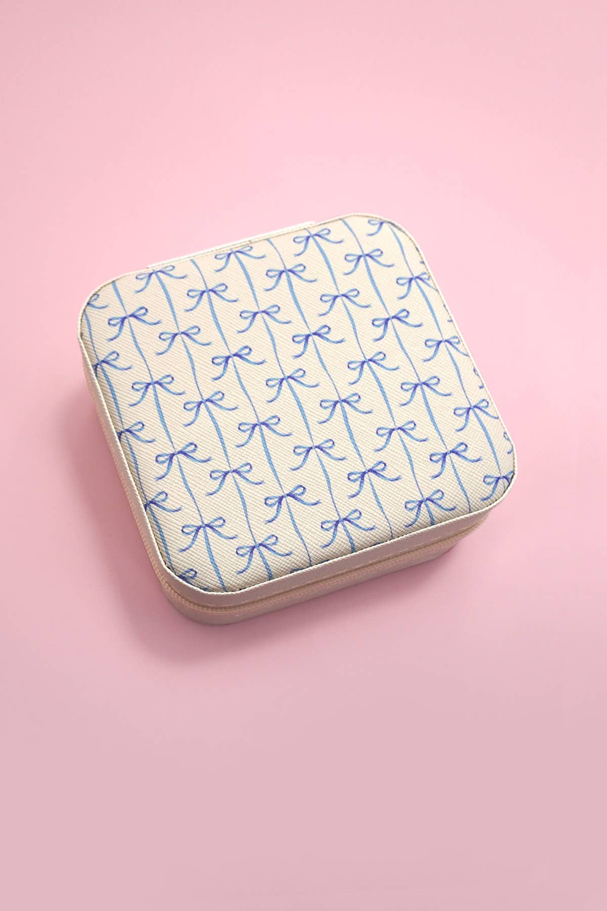 Square cream jewelry case with blue bow pattern on pink background