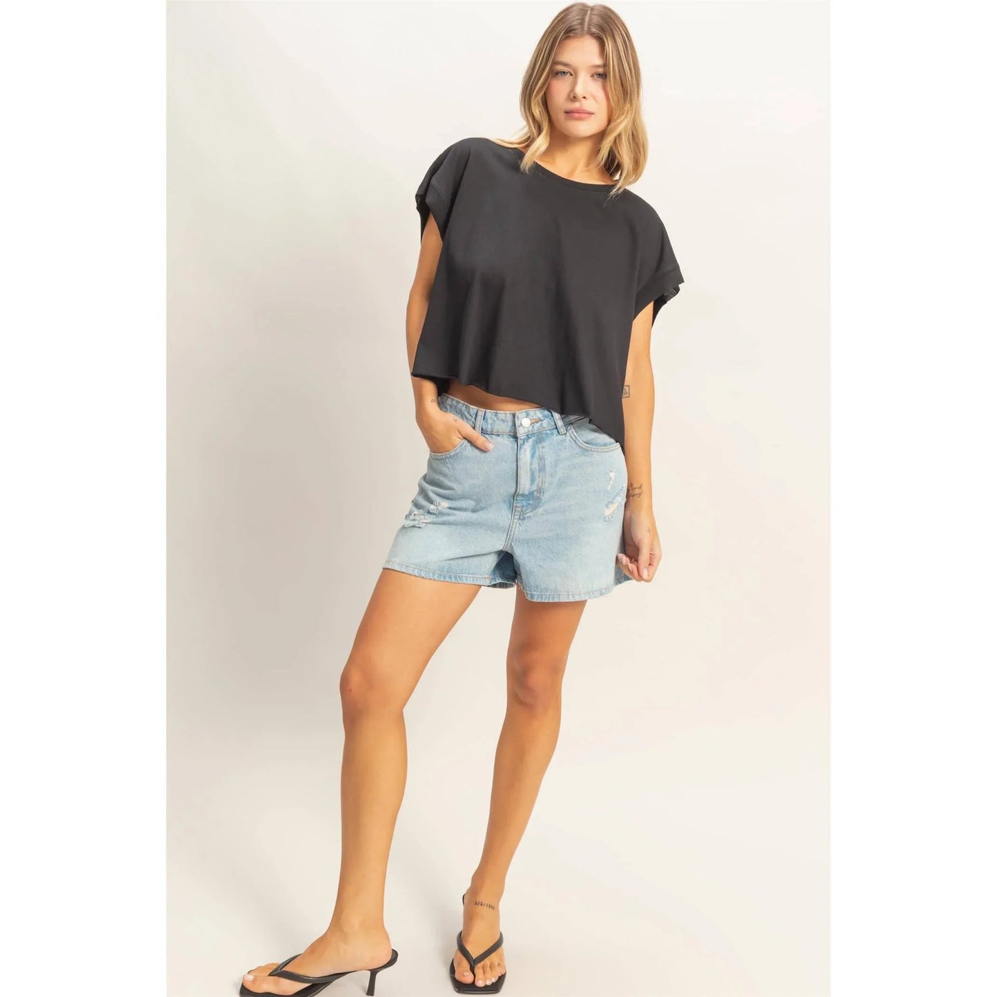 Woman wearing a black cropped t-shirt and distressed light wash denim shorts