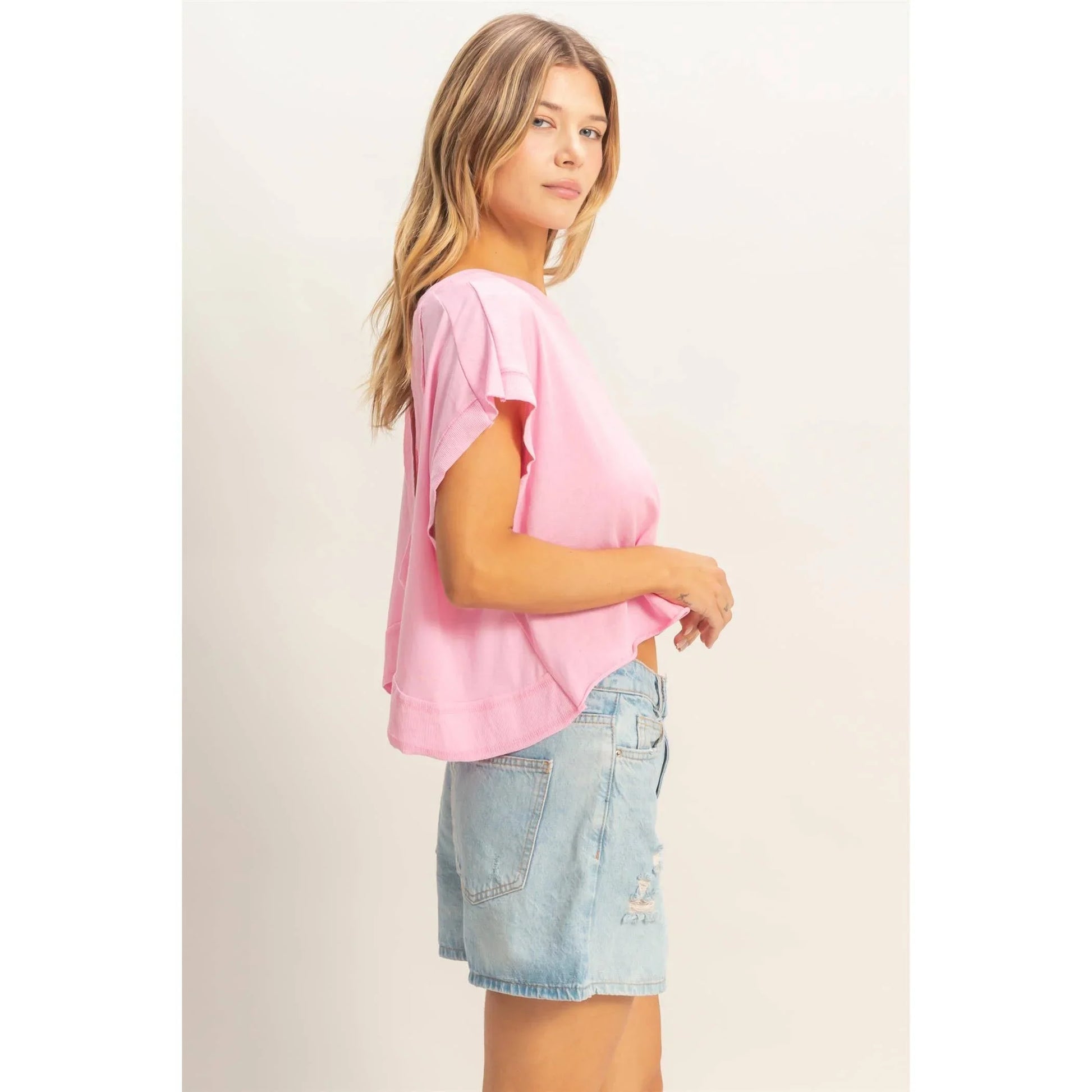 Woman wearing loose pink t-shirt and high-waisted denim shorts on white background
